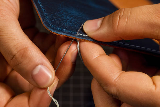 Hands stitching the edge of a leather wallet with needle and thread